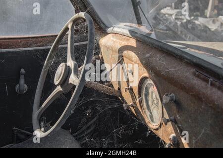 Nahaufnahme eines alten rostigen Retro-Autos. Es ist ein Linkslenker und zeigt Lenkrad und Armaturenbrett mit Rost und Spinnweben bedeckt Stockfoto