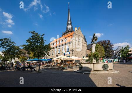 Deutschland, Ratingen, Bergisches Land, Rheinland, Nordrhein-Westfalen, NRW, Marktplatz, im Bürgerhaus, ehemaliges Rathaus, hinter der katholischen Pfarrkirche St. Peter und Paul, vor der Marktquelle von Hans Breker mit Löwenfigur auf einer Säule sitzen Menschen in einem Gehsteig-Restaurant Stockfoto