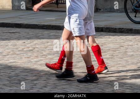 Zwei Schuljungen, die in Sportkleidung eine gepflasterte Straße entlang gehen - Nahaufnahme ihrer Beine in roten Fußballsocken und weißen Shorts Stockfoto