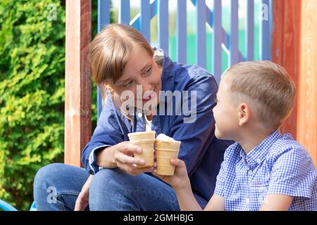 Vorschulkinder Junge mit Mama essen Eis auf der Veranda eines Hauses im Dorf an einem sonnigen Sommertag. Selektiver Fokus. Hochformat Stockfoto