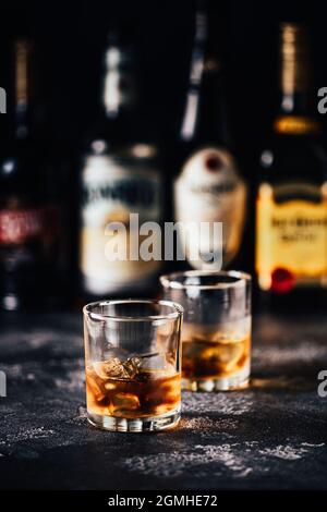 Whiskey mit Eis auf einem dunklen Tisch vor dem Hintergrund von Barflaschen Stockfoto