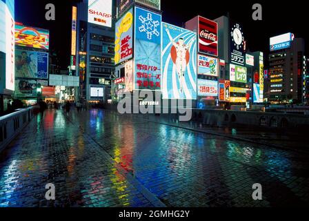 Japan. Stadt Osaka bei Nacht. Neon-Werbeschilder spiegeln sich auf nassem Pflaster wider. Stockfoto