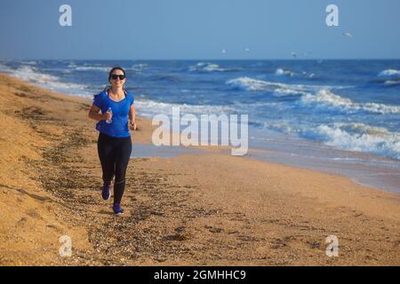 Frau, die am Strand am Meer läuft und Musik hört Stockfoto