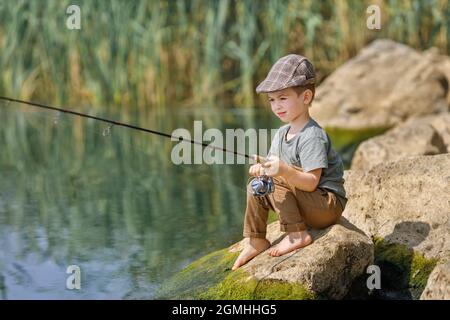 Kleiner Junge sitzt auf Stein und fischt Stockfoto