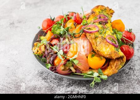 Omelette mit geschmortem Gemüse und Lachs, Tomaten mit Zwiebeln, Brokkoli und rotem Fisch mit Erbsen-Microgreens, leckeres herzhaftes Frühstück Stockfoto