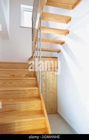 Moderne Holztreppe mit Geländern und Stauraum, vom ersten bis zum zweiten Stock. Vertikales Bild. Stockfoto