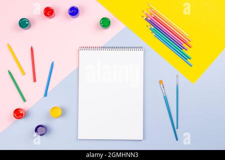 Kreative Kunstwerke liefern Hintergrund. Aquarell, Pinsel, Bleistifte, offenes leeres Notizbuch auf hellgrauem Tisch. Draufsicht, flach liegend Stockfoto