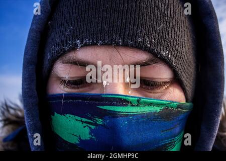 Nahaufnahme eines kaukasischen Männergesichts mit Schal als Maske und Kapuzenjacke mit Frost auf den Augenbrauen Stockfoto