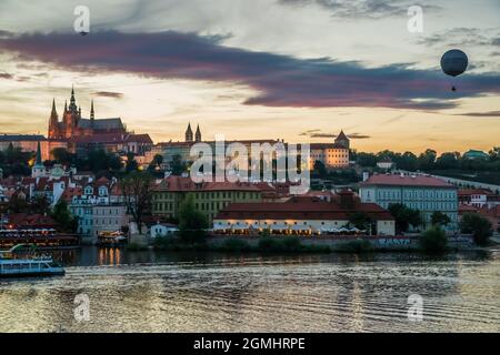 PRAG, TSCHECHISCHE REPUBLIK - 28. AUGUST 2012: Blick über die Moldau auf die Prager Burg bei Sonnenuntergang mit einem Ballon am Himmel. Stockfoto