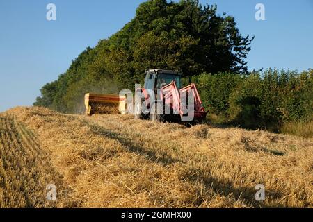 Ein Traktor zieht eine Ballenpresse über ein Herefordshire-Feld, um Strohballen herzustellen, nachdem die Gerstenkornernte kombiniert wurde Stockfoto