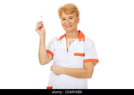 Eine leitende Ärztin, die eine weiße und orangefarbene Uniform trägt und eine Spritze auf weißem Hintergrund hält Stockfoto