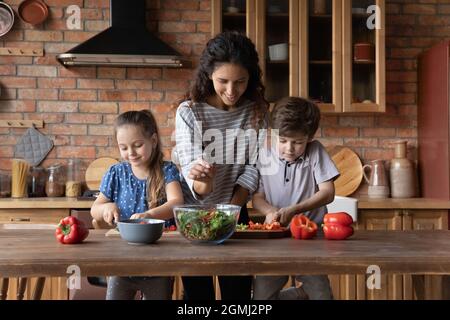 Glückliche junge Mutter, die mit Kindern Essen zubereitete. Stockfoto