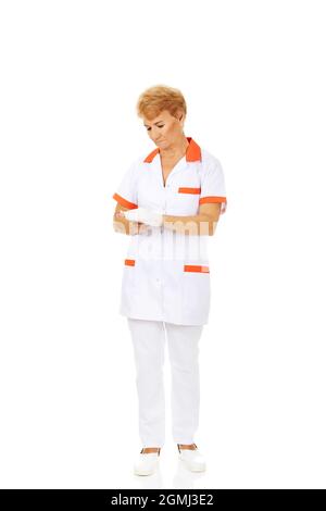 Eine ältere Ärztin, die eine weiße und orangefarbene Uniform trägt und ihre Hand verband Stockfoto