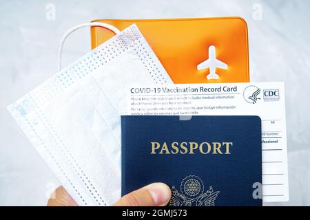 US-Pass mit einer Covid-19-Impfkarte, Gesichtsmaske und Dokumenten-Organisator in der Hand. Pandemie-Zeitreisekonzept. Stockfoto