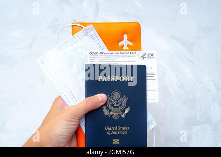 Hand mit einem US-Pass mit einer Impfkarte, Gesichtsmaske und einem Organizer in der Hand. Internationale Reisen während des Covid-19. Stockfoto