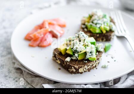 Gesundes Frühstück mit Lachs und Toast mit Roggenbrot, Avocado und Blauschimmelkäse. Stockfoto