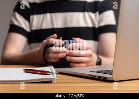 Ein Mann, der mit einem Computer-Laptop arbeitet und in der Hand noch eine Tasse Kaffee hält.Konzept Arbeit von zu Hause, zu Hause bleiben. Hochwertige Fotos Stockfoto