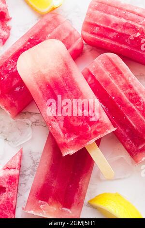 Hausgemachte Wassermelone-Eiszapfen mit weißem Marmorhintergrund. Eiszapfen aus gefrorener Wassermelone. Sommerkonzept. Draufsicht. Stockfoto
