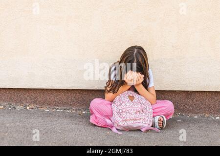 Kleine Brünette Mädchen versteckt Gesicht mit Händen, allein sitzen und traurig fühlen Stockfoto