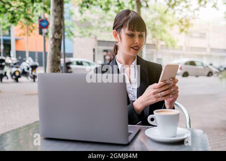 Porträt einer schönen Geschäftsfrau mit Laptop im Café im Freien sitzen und mit dem Smartphone Stockfoto
