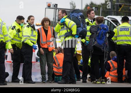 Enfield, Großbritannien. September 2021. Ein Polizeibeamter der Metropolitan Police verhaftete einen beleidigenden britischen Klimaaktivisten, der im Rahmen einer Kampagne, die die britische Regierung dazu bewegen sollte, erhebliche Gesetzesänderungen vorzunehmen, um die Emissionen zu senken, eine Zufahrtsstraße der M25 an der Kreuzung 25 blockiert hatte. Die Aktivisten, Die am 13. August an Premierminister Boris Johnson geschrieben haben, fordern, dass die Regierung unverzüglich verspricht, sowohl die vollständige Finanzierung als auch die Isolierung des gesamten sozialen Wohnungsbaus in Großbritannien bis 2025 sicherzustellen und innerhalb von vier Monaten einen rechtsverbindlichen nationalen Plan zur vollständigen Finanzierung und Sicherstellung des zu erstellen Stockfoto