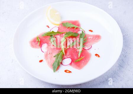 Frischer Thunfisch-Carpacio mit Rucola, Rettich, Chili und Zitrone. Traditionelle kalte Vorspeise der italienischen Küche. Nahaufnahme, selektiver Fokus. Stockfoto