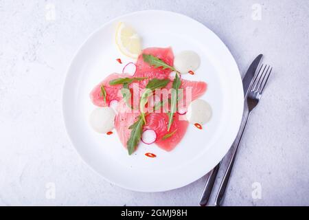 Frischer Thunfisch-Carpacio mit Rucola, Rettich, Chili, Zitrone und Sauce. Traditionelle kalte Vorspeise der italienischen Küche. Nahaufnahme, selektiver Fokus, Draufsicht. Stockfoto