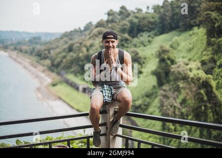 Kerl mit einem Tattoo am ganzen Arm sitzt auf dem Geländer auf der Aussichtsplattform im Dschungel. Landschaftlich schöner Blick in Georgien. Hochwertige Fotos Stockfoto