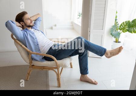 Unbeschüttelter Tausendjähriger Single-Mann, der sich auf einem Stuhl in einem modischen Zuhause entspannt Stockfoto