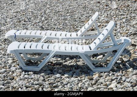 Zwei weiße Sonnenliegen am Kiesstrand im Sommer. Hochwertige Fotos Stockfoto