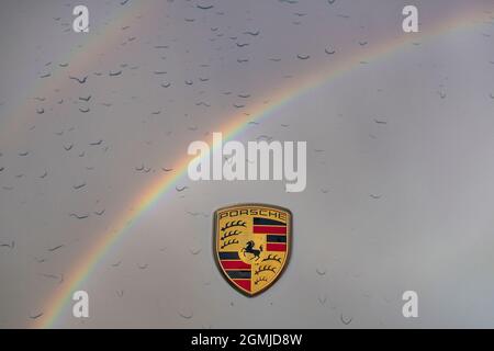 Porsche-Abzeichen auf der Motorhaube von 911 mit Tröpfchen Regenwasser und Regenbogenreflektion Stockfoto