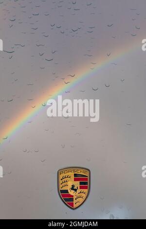 Porsche-Abzeichen auf der Motorhaube von 911 mit Tröpfchen Regenwasser und Regenbogenreflektion Stockfoto