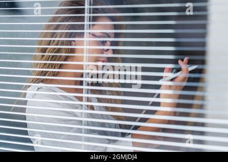 Die junge, schöne Geschäftsfrau hält ein mobiles Tablet an der Hand, um ihre Arbeit zu überprüfen, während sie neben Fenstern steht. Stockfoto