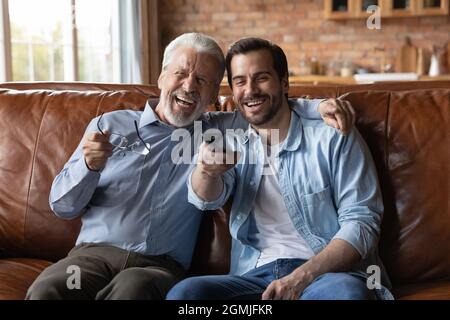 Lachender junger Mann mit reiferem Vater, der zusammen Fernsehen schaut Stockfoto