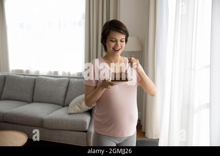 Hungrige Millennial-Schwangeren genießen es, leckeren Kuchen zu essen Stockfoto