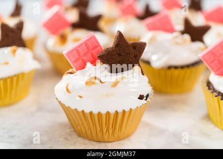 Gourmet-S'mores-Cupcakes mit Meringue-Zuckerguss und garniert mit sternförmiger Schokolade graham Cracker und einer pinken Mini-Tafel Schokolade. Stockfoto