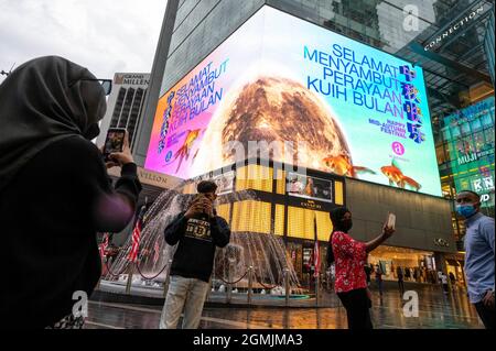 Kuala Lumpur, Malaysia. September 2021. Menschen posieren für Fotos vor einem Bildschirm, auf dem ein Video zur Feier des bevorstehenden Herbstfestes in einem Einkaufszentrum in Kuala Lumpur, Malaysia, am 19. September 2021, gezeigt wird. Quelle: Chong Voon Chung/Xinhua/Alamy Live News