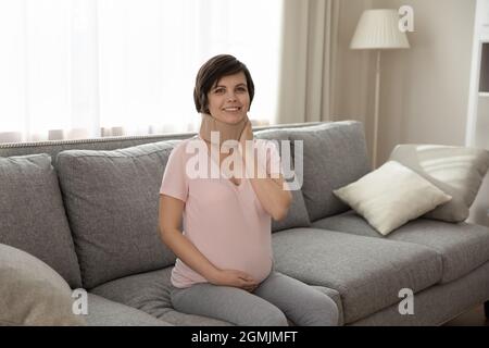 Frau mit fortgeschrittener Schwangerschaft sitzen auf dem Sofa im medizinischen Kragen Stockfoto