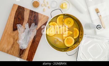 Rezept für geröstete putenschenkel mit Kräutern. Marinade für putenfleisch aus nächster Nähe in einem Topf. Orangensaft, Orangenscheiben, Knoblauch und Gewürze - Zutaten in der Küche Stockfoto