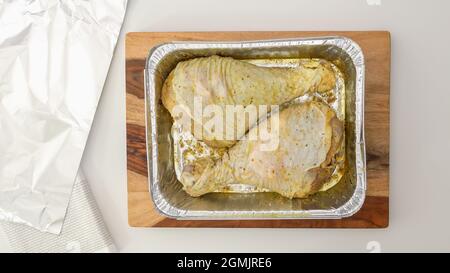 Rohe marinierte putenbeine in Backform, fertig gekocht. Flach liegend, weißer Küchentisch Hintergrund Stockfoto