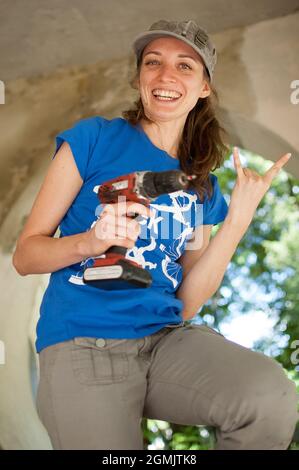 Qualifizierte junge Arbeiterin verwendet Power-Schraubendreher Bohren während der Konstruktion Holzbank Geschlechtergleichheit, Feminismus, tun Sie es selbst Konzepte. Stockfoto