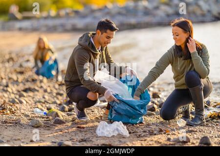 Team engagierter und lächelnder Freiwilliger, die Plastikmüll am Strand sammeln Stockfoto