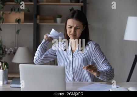 Verärgerte frustrierte Geschäftsfrau, die zerknitterte Papiere auf den Laptop-Bildschirm warf Stockfoto