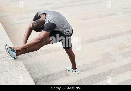 Afrikanischer junger Mann, der Stretching-Übungen während des Sporttrainings im Freien macht Stockfoto