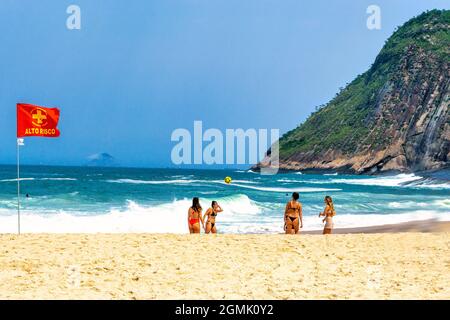 Rote Flagge und Touristen genießen den Strand von Itacoatiara in Niteroi, Rio de Janeiro, Brasilien. Mit einer wunderschönen Landschaft ist dieser Strand berühmt für seine Angebote Stockfoto