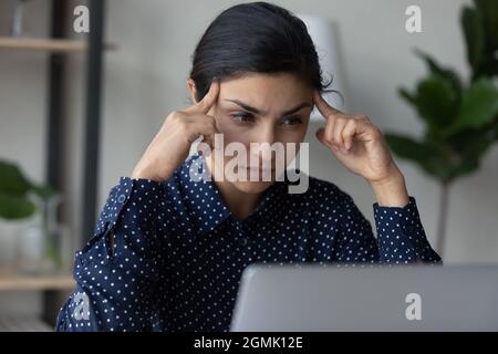 Nahaufnahme einer nachdenklichen indischen Geschäftsfrau, die mit einem Laptop die Tempel berührt Stockfoto