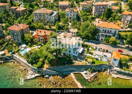 Schöne Villen in der Nähe der Küste von felsigen Strand in einer kleinen Stadt Lovran, Kroatien. Arial Blick auf Lungomare Meer Gehweg mit transparentem Wasser. Stockfoto