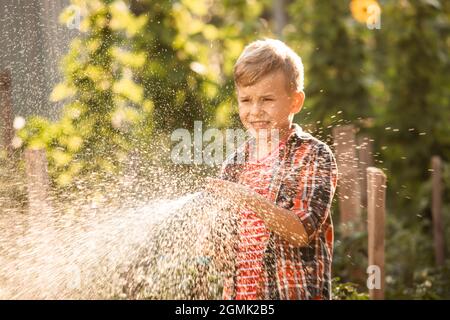 Der kleine Junge wäscht die Pflanzen und macht große Wasserspritzer Stockfoto