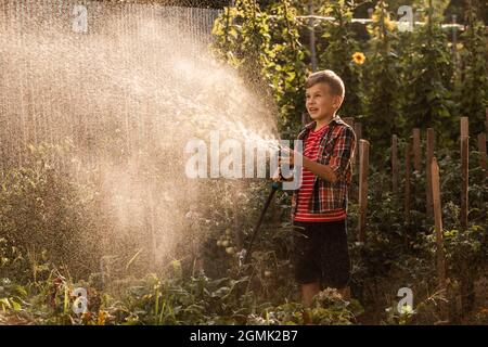 Der kleine Junge wäscht die Pflanzen und macht große Wasserspritzer Stockfoto