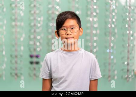 Ein asiatischer Junge, der in einem Optikerladen an einer Brille versucht. Stockfoto